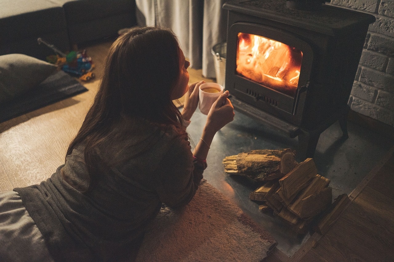 Logs In Essex | Woman warming by fire with hot drink